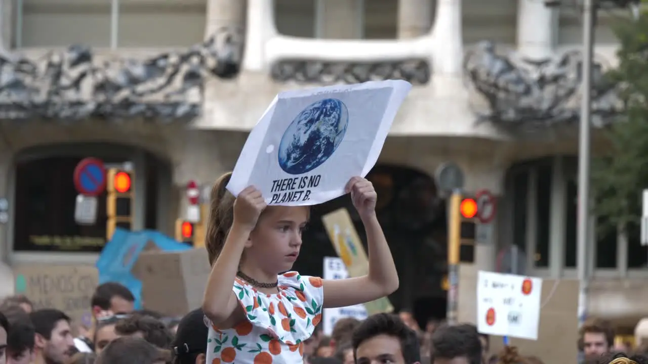 Little girl holds climate change protest sign above crowd riding on shoulders