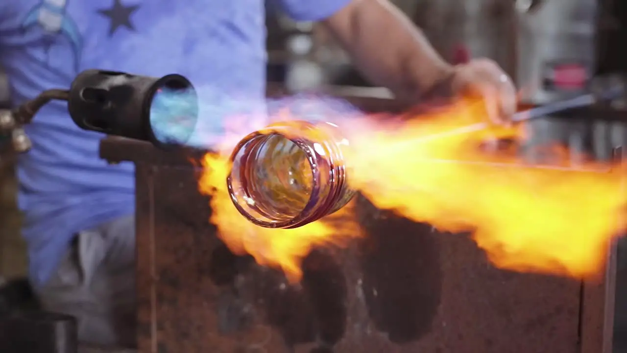 A glass blower heating a whiskey glass with fire flames