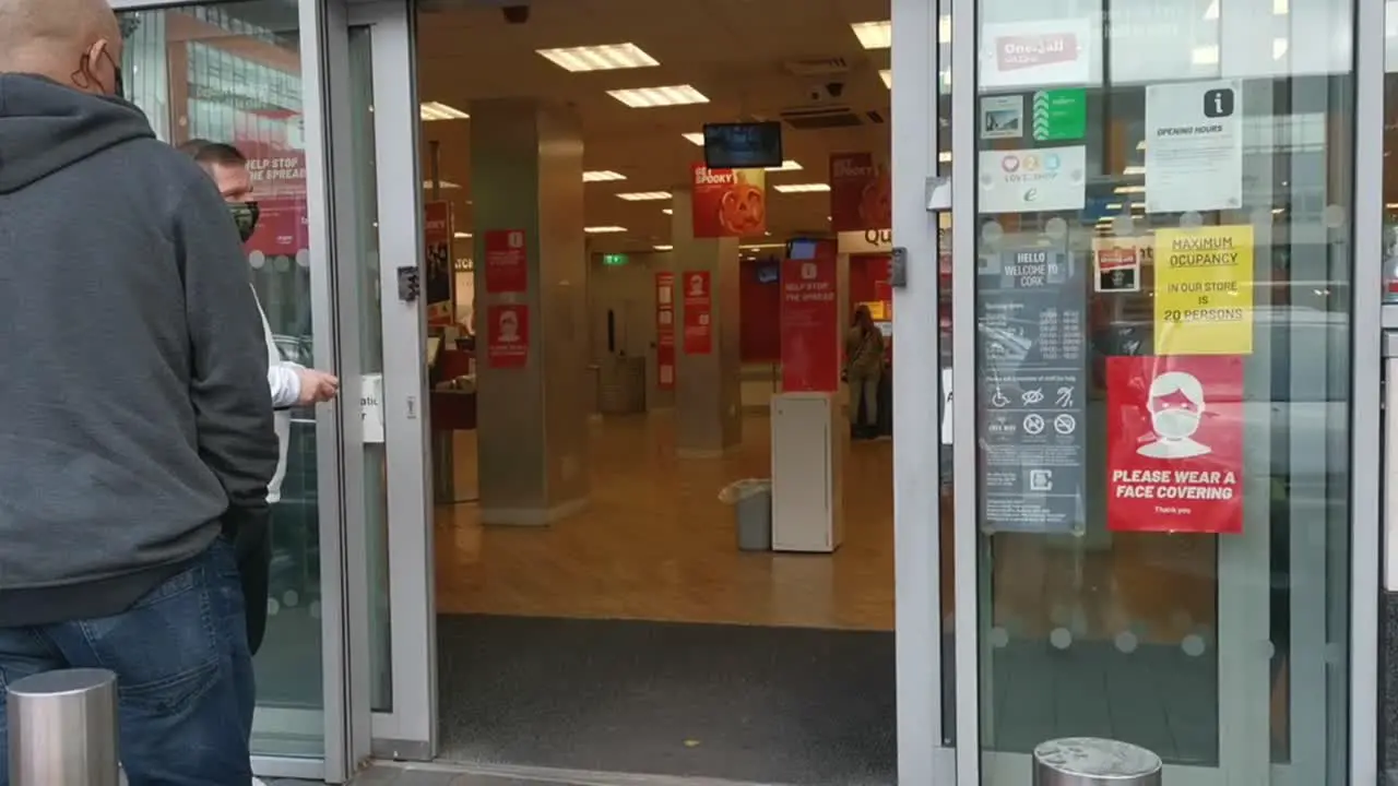 People standing in front of the shop with face masks with warning signs about distance and face masks on doors