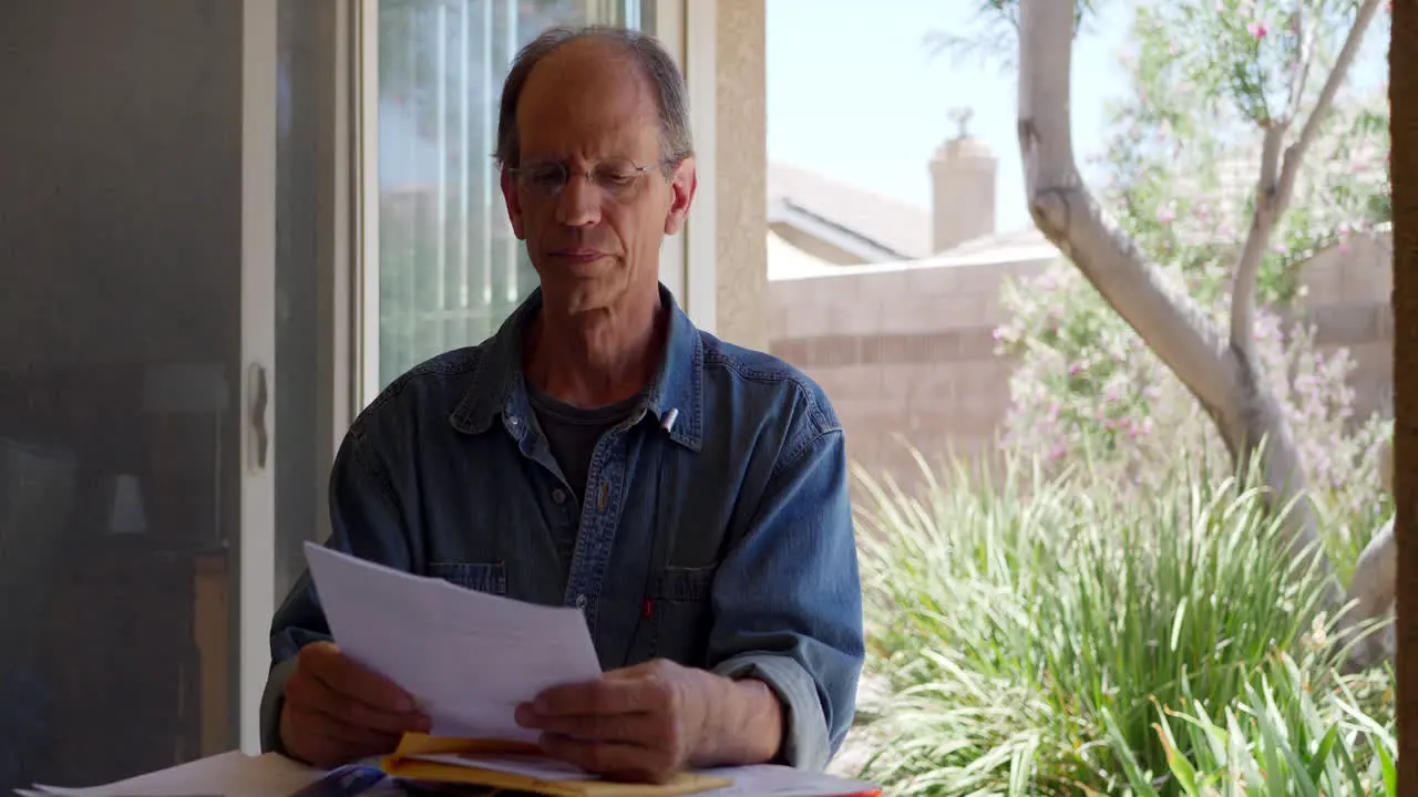 An older middle aged man reading a medical letter giving him bad news that he has been diagnosed with cancer and looking calm and sad but remaining hopeful positive and optimistic