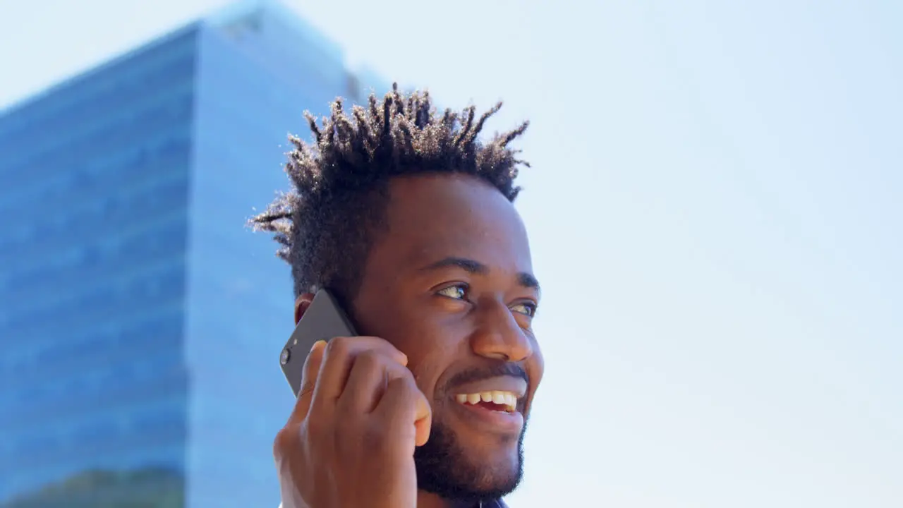 Low angle view of young black businessman talking on mobile phone in balcony of modern office 4k