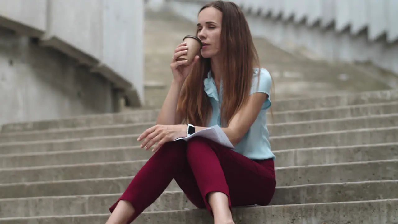 Businesswoman with documents sitting on stairs Employee drinking coffee to go