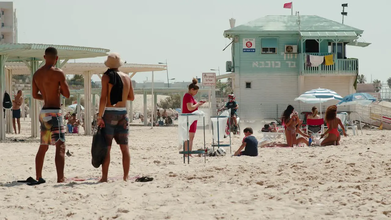 Cheeky punk drives aggressively on a dirt bike among the innocent people on an Israeli beach in Ashkelon saying hello to his friend