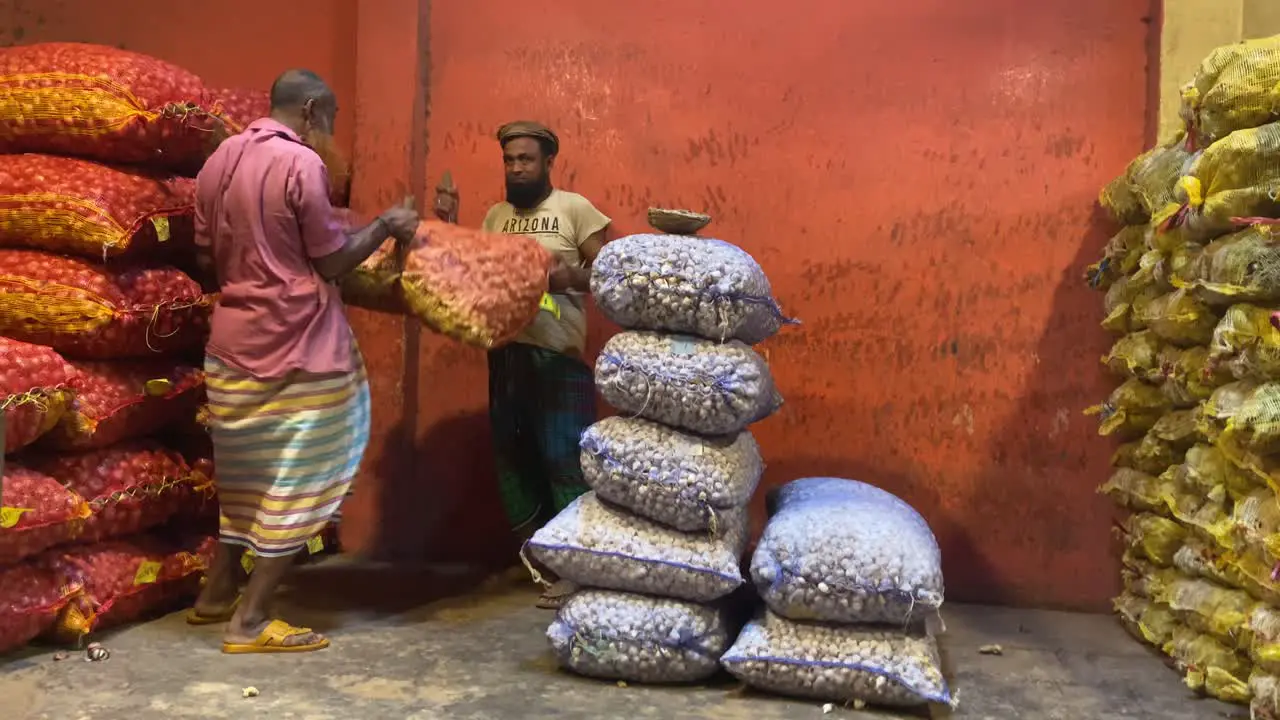 2 workers lifting then carrying a sack of ginger onion garlic on his head from inside a storage area to outside