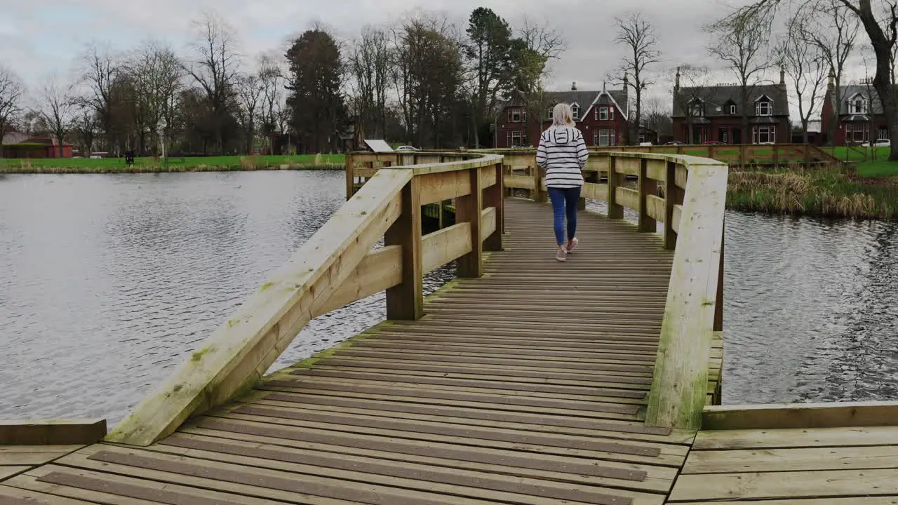 A young woman walks over a bridge in a local park