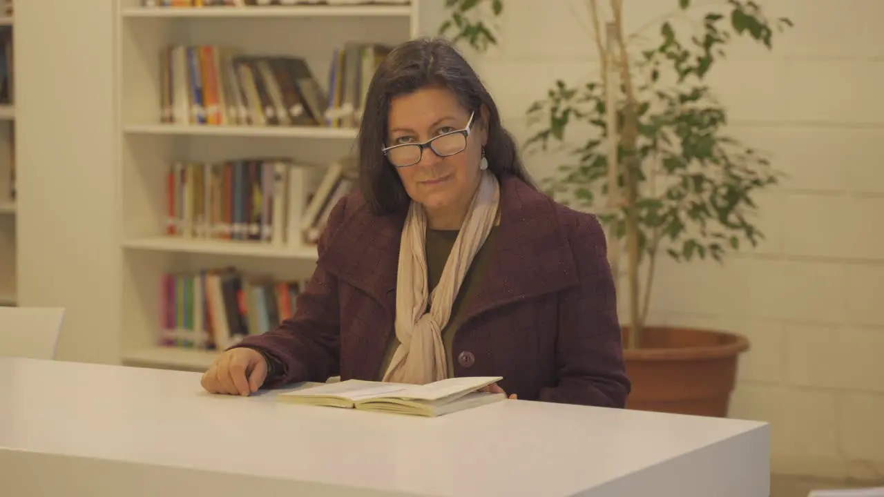 Beautiful middle aged woman sitting in library smiles while looking at camera