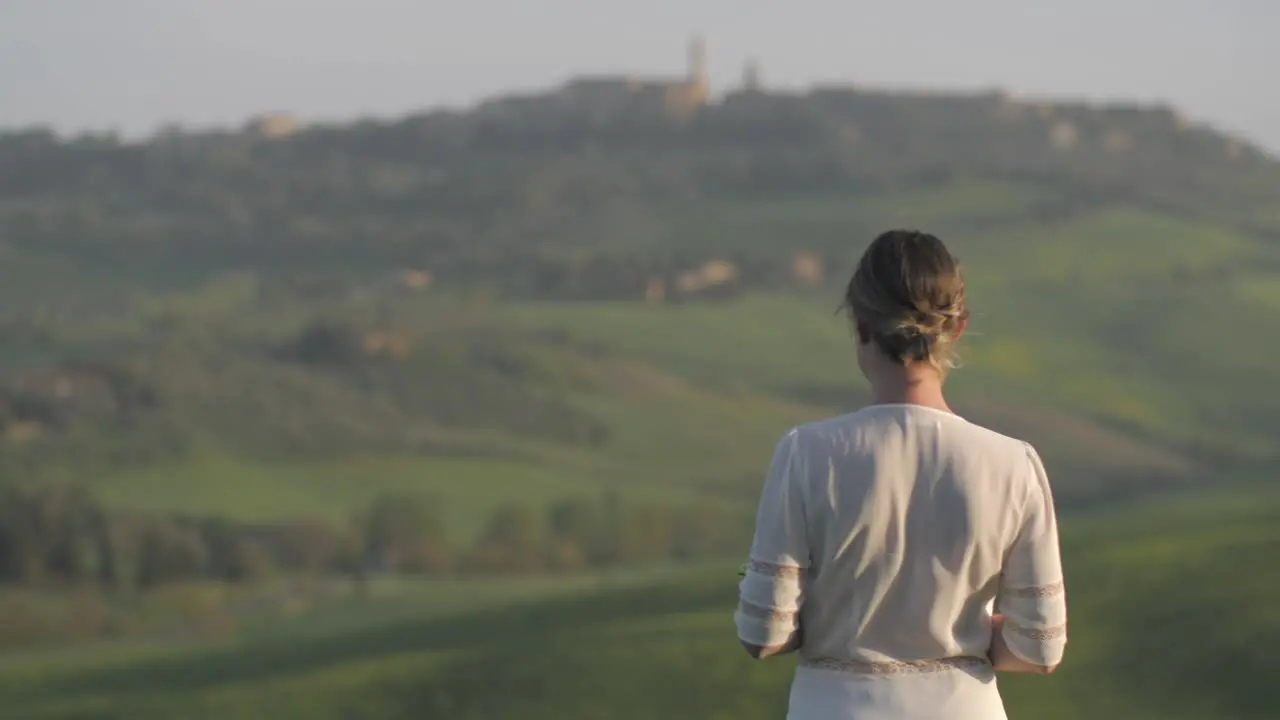 Young woman dressed in white calmy standing in Tuscan field wind gently blows