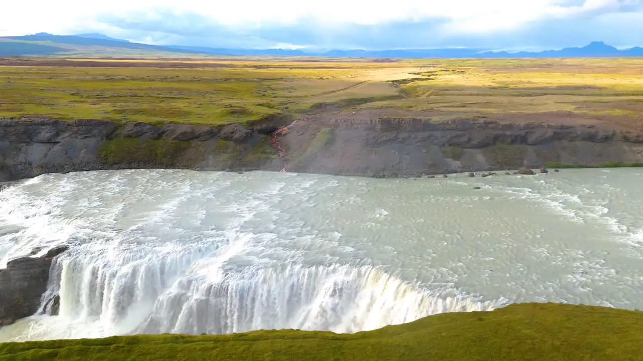 Aerial drone tracking shot over a large Icelandic plain with a river in the foreground and a large impressive waterfall called gulfoss