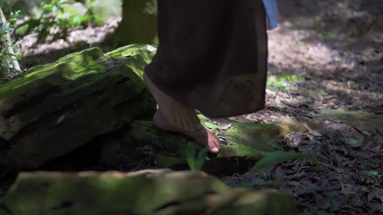 Brunette woman walking on the slatted stones of a lush forest with bare feet wearing a brown dress