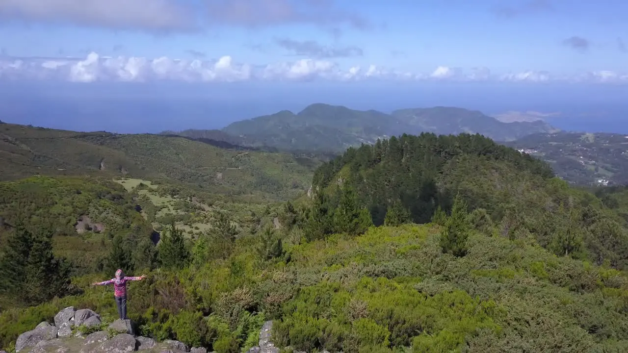 A man standing on a high view point of the Madeira mountains in Portugal and raising his arms to mother nature Aerial shot