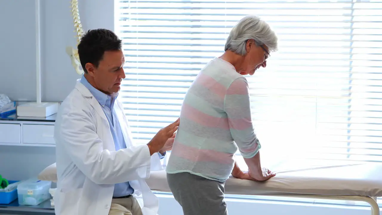 Physiotherapist giving back massage to senior patient