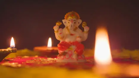 Hand Arranging Diya Lamps Around Statue Of Ganesh On Table Decorated For Celebrating Festival Of Diwali 1