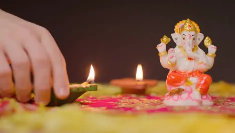 Hand Arranging Diya Lamps Around Statue Of Ganesh On Table Decorated For Celebrating Festival Of Diwali