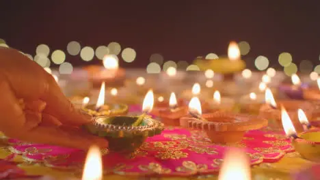 Person Putting Burning Diya Lamp Onto Table Decorated To Celebrate Festival Of Diwali