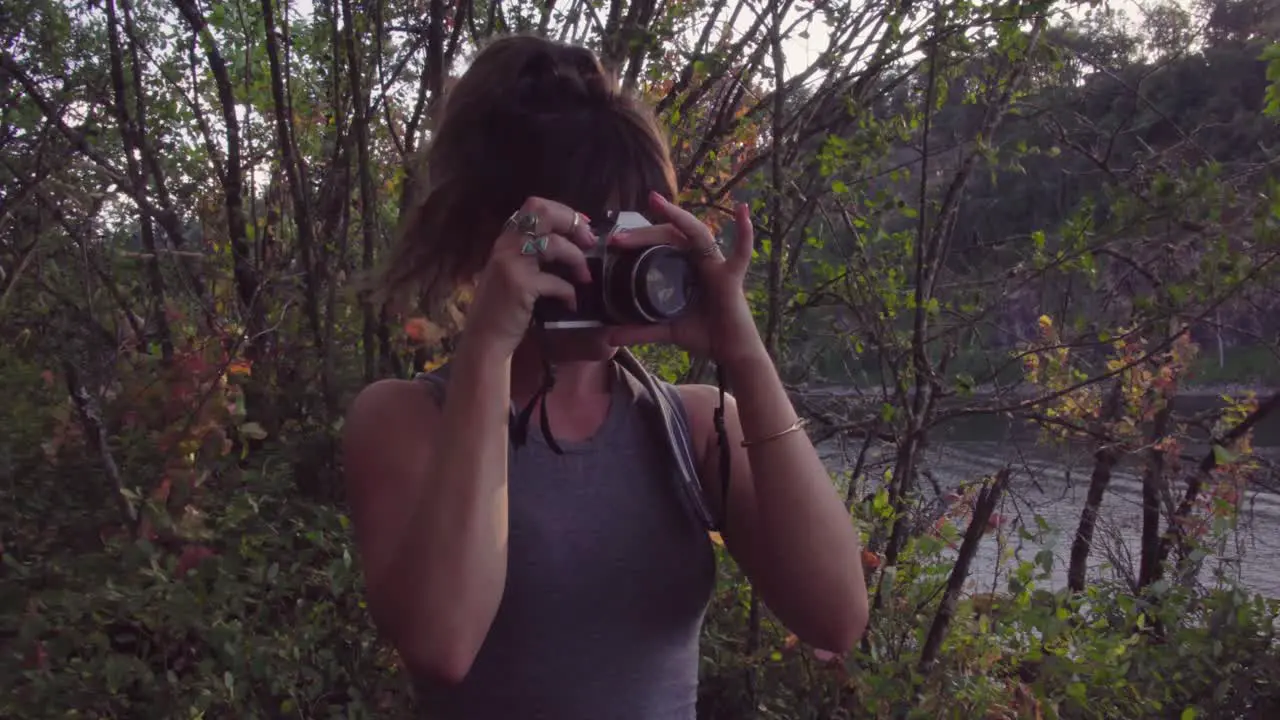 Cute hipster girl in a park focusing a film camera to take a photo