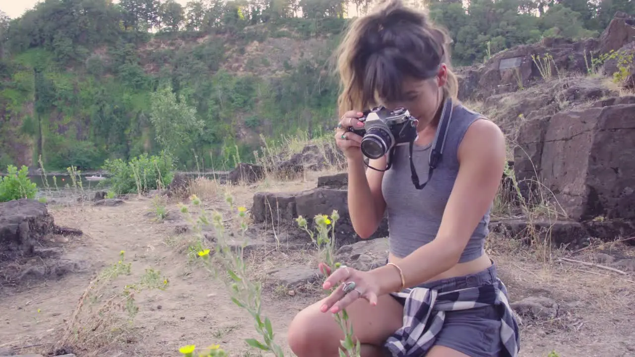 Cute hipster girl taking photos of flowers on a film camera