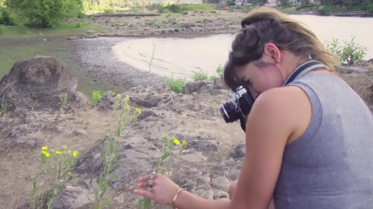 A cute hipster girl taking photos of flowers on a film camera