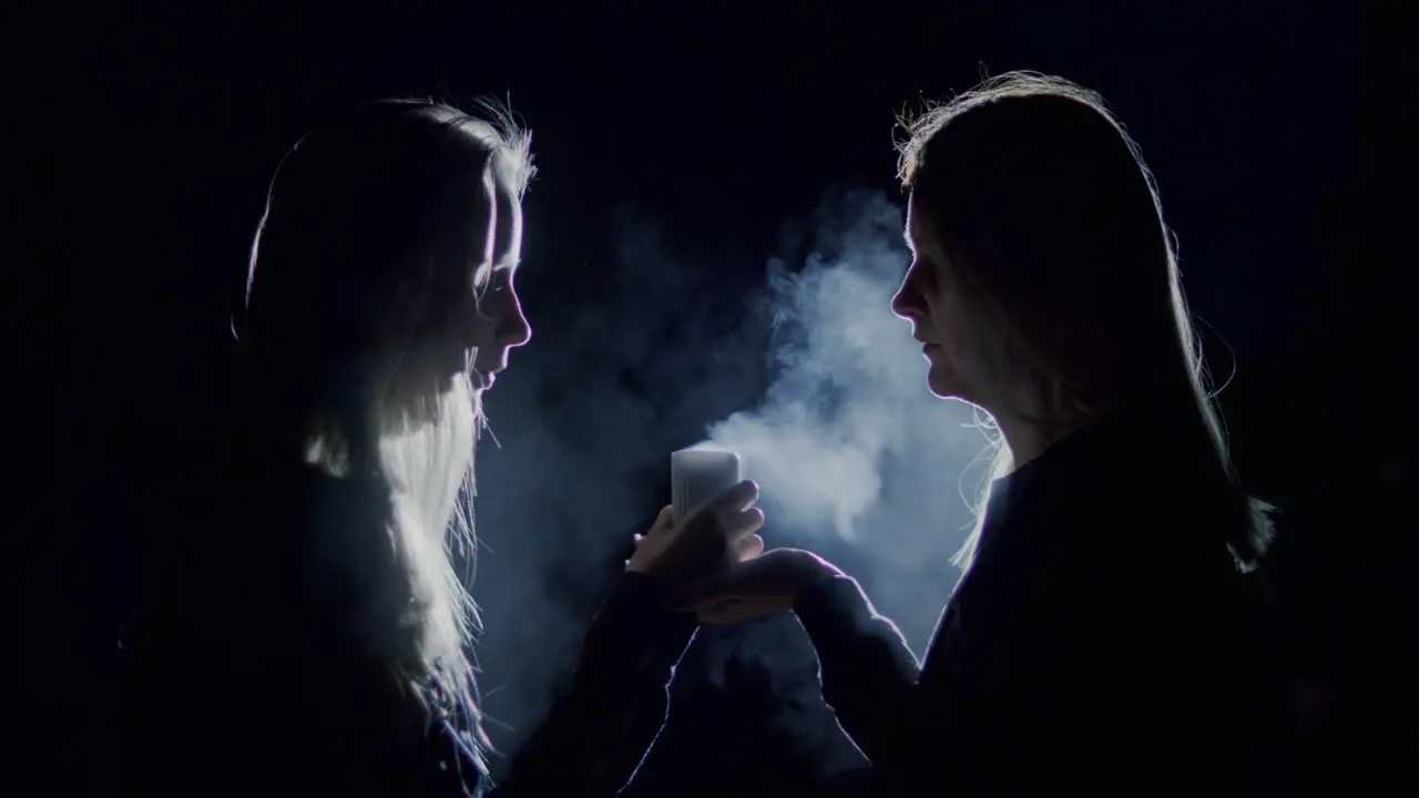 A woman and a teenage girl sit side by side and look at a candle burning in the dark