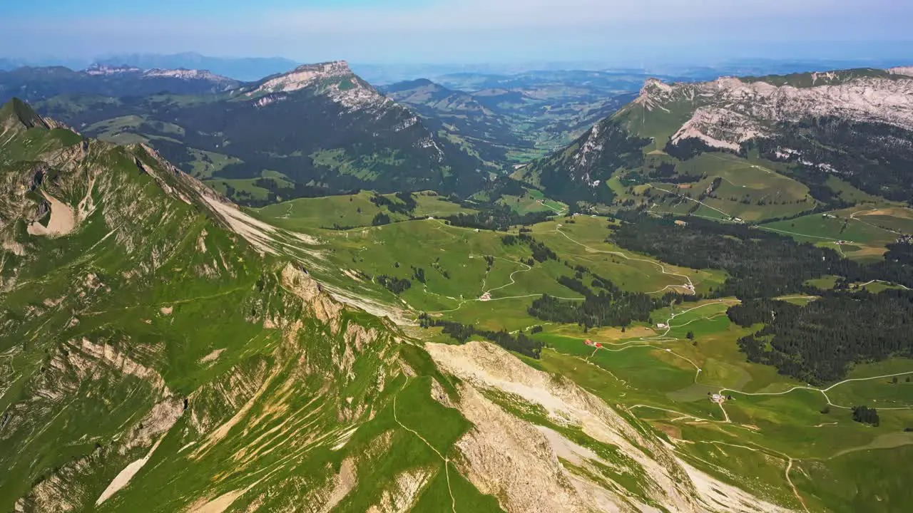 Aerial view of a vast mountain range and a blue sky than pans down to reveal a high peak that slopes down to a valley