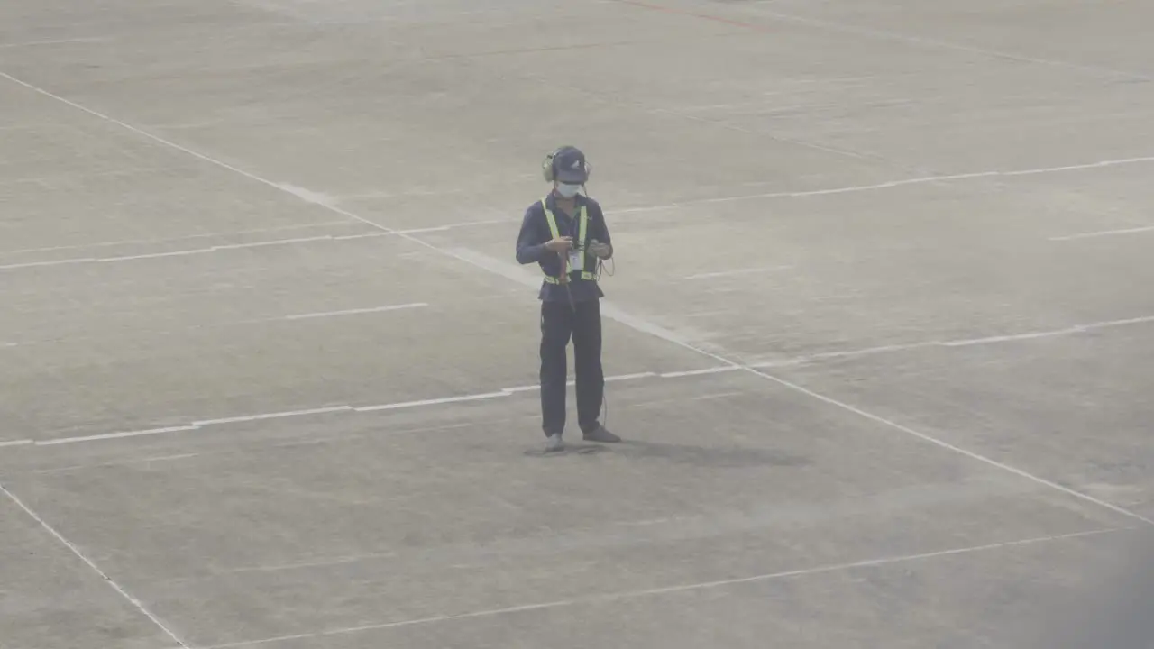 A dedicated airport worker in uniform stands on the tarmac surrounded by concrete  ready to assist pilot in take off