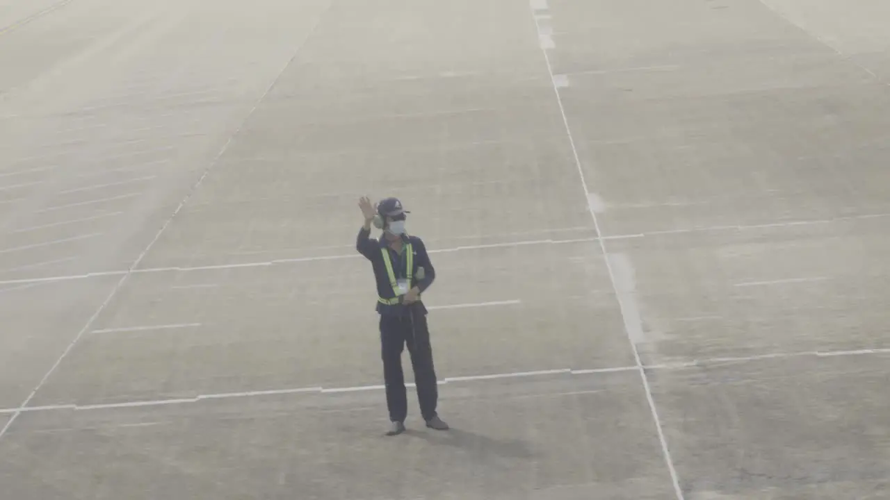 A dedicated airport worker in uniform waves good bye to the pilot while take off