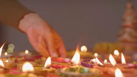 Person Putting Burning Diya Lamp Onto Table Decorated To Celebrate Festival Of Diwali 3