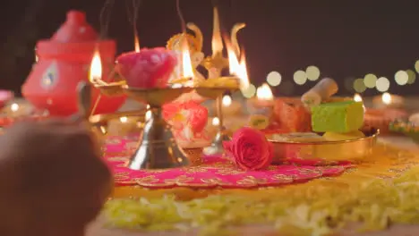 Person Holding Five Wick Lamp And Statue Of Ganesh On Decorated Table Celebrating Festival Of Diwali