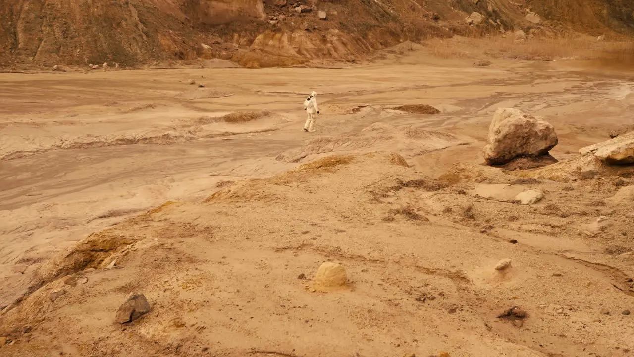 Wide shot of an astronaut wearing a spacesuit moving across a deserted planet with red soil and rocks looks off into the distance