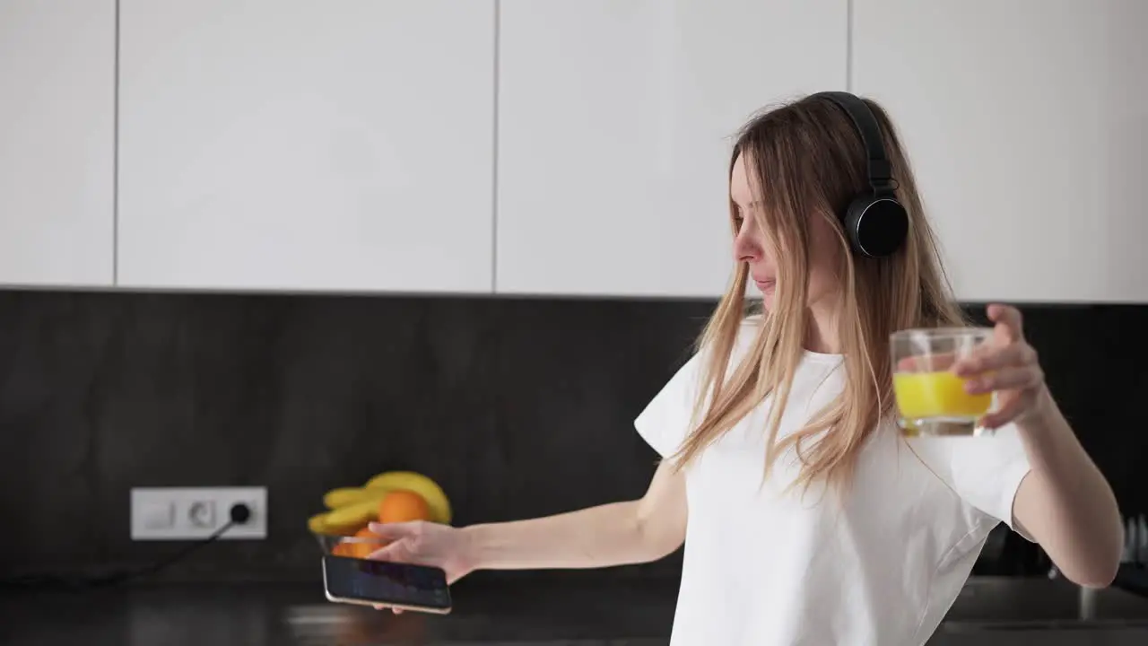 A Young Woman Is Dancing In The Kitchen And Drinking Juice