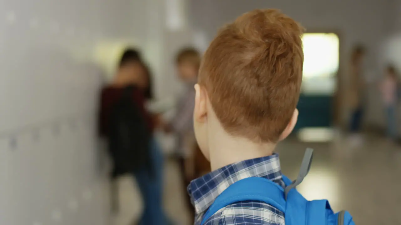 Portrait Of The Little Cute Red Haired Schoolboy With Schoolbag Turning His Head To The Camera And Smiling Straight To It At The School Corridor