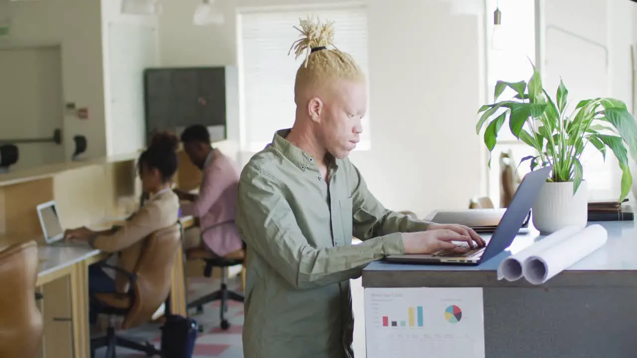 Portrait of happy albino african american businessman using laptop in creative office