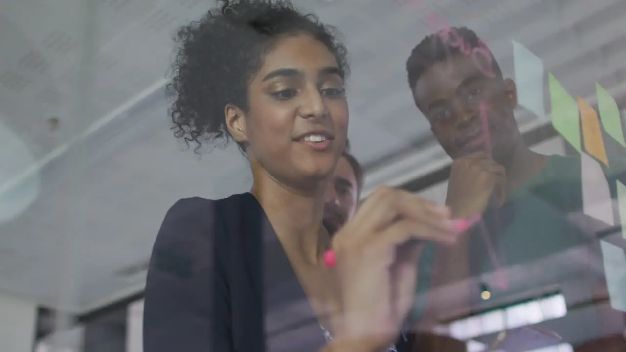 Diverse colleagues using memo notes and writing on glass wall having a discussion