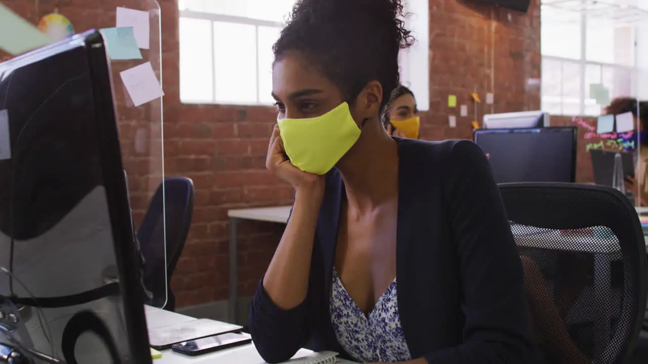 Mixed race businesswoman having video chat sitting in front of computer wearing face mask