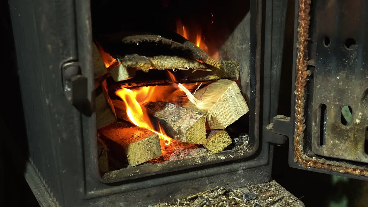 Burning firewood in small metal fireplace for heating close up view