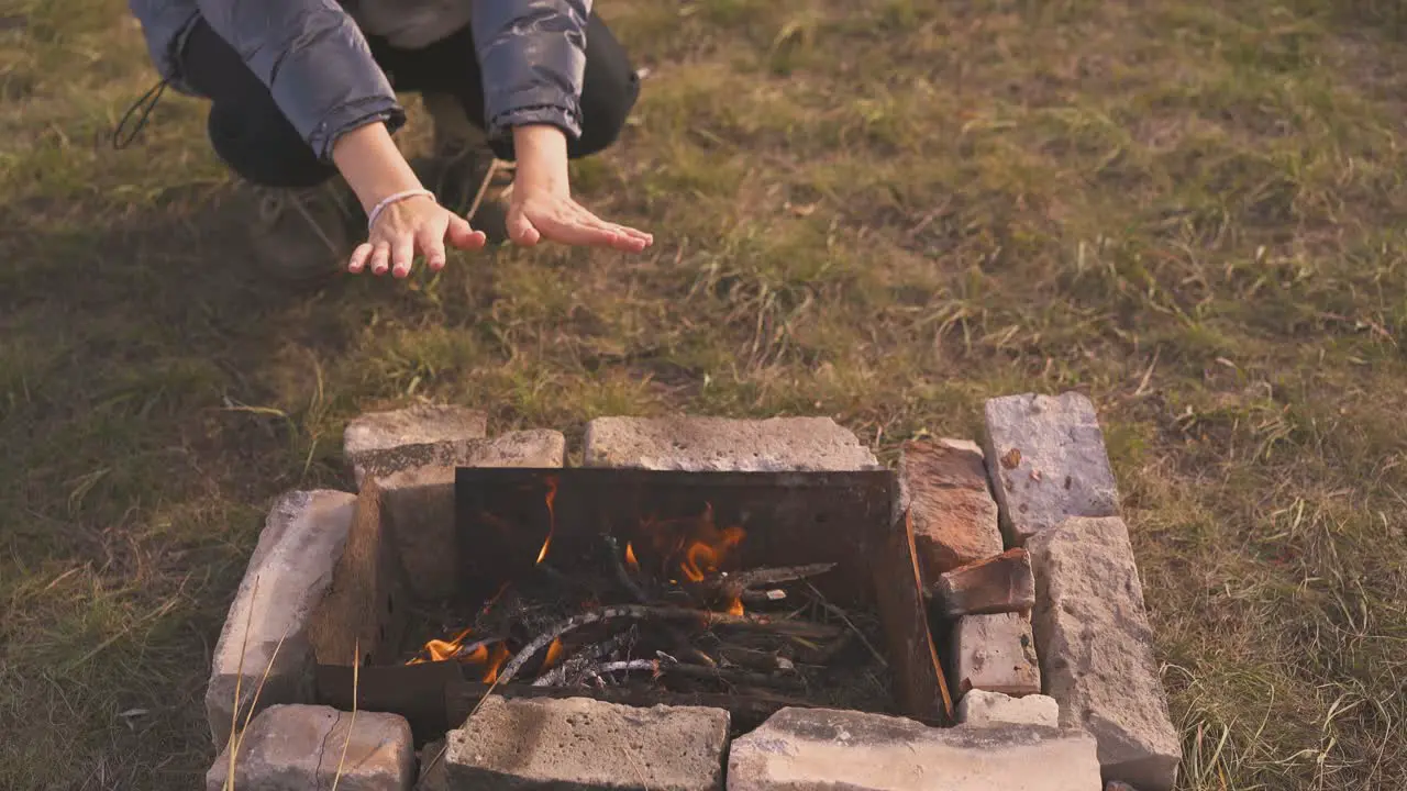 woman tourist heats palms at bonfire with bricks closeup