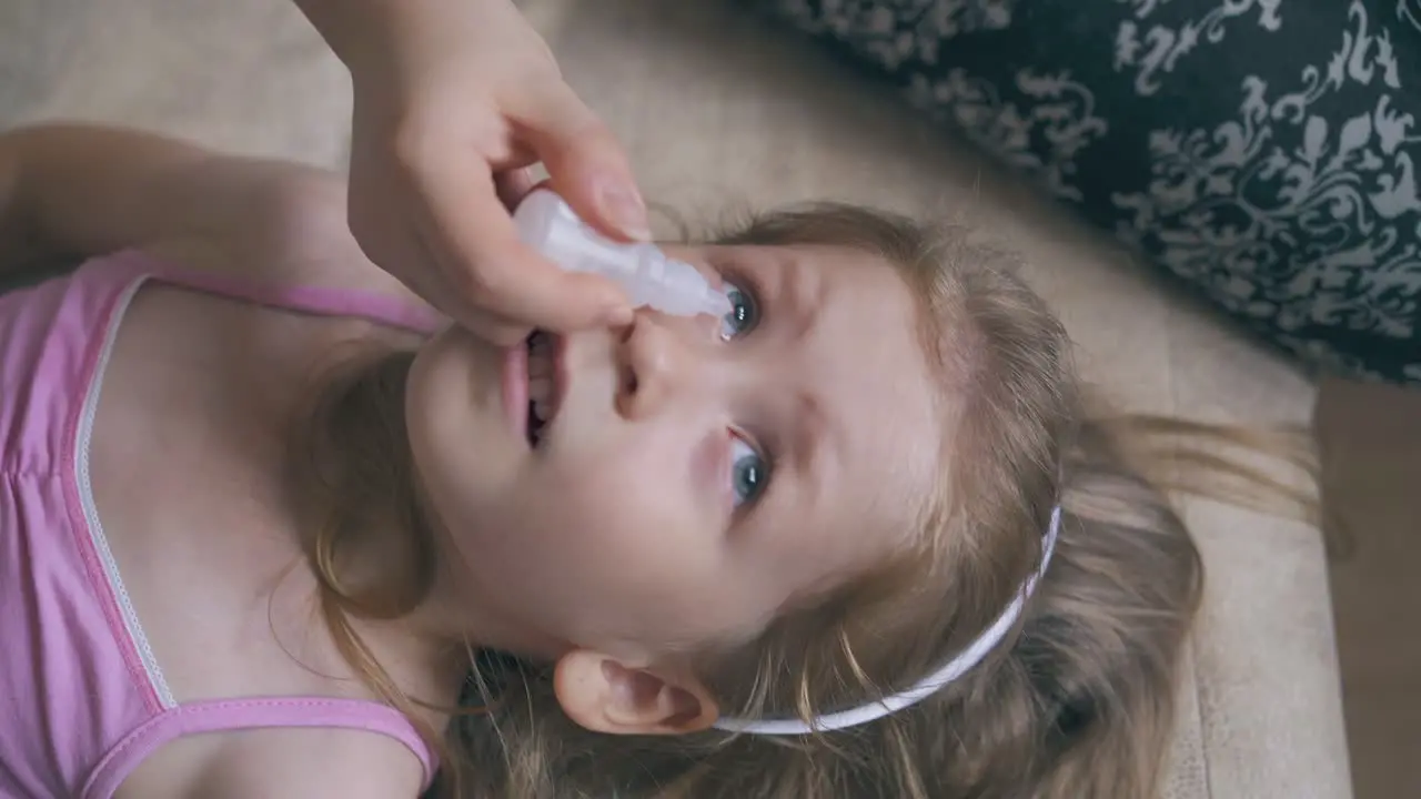 woman gives eye drops to little girl lying on soft bed