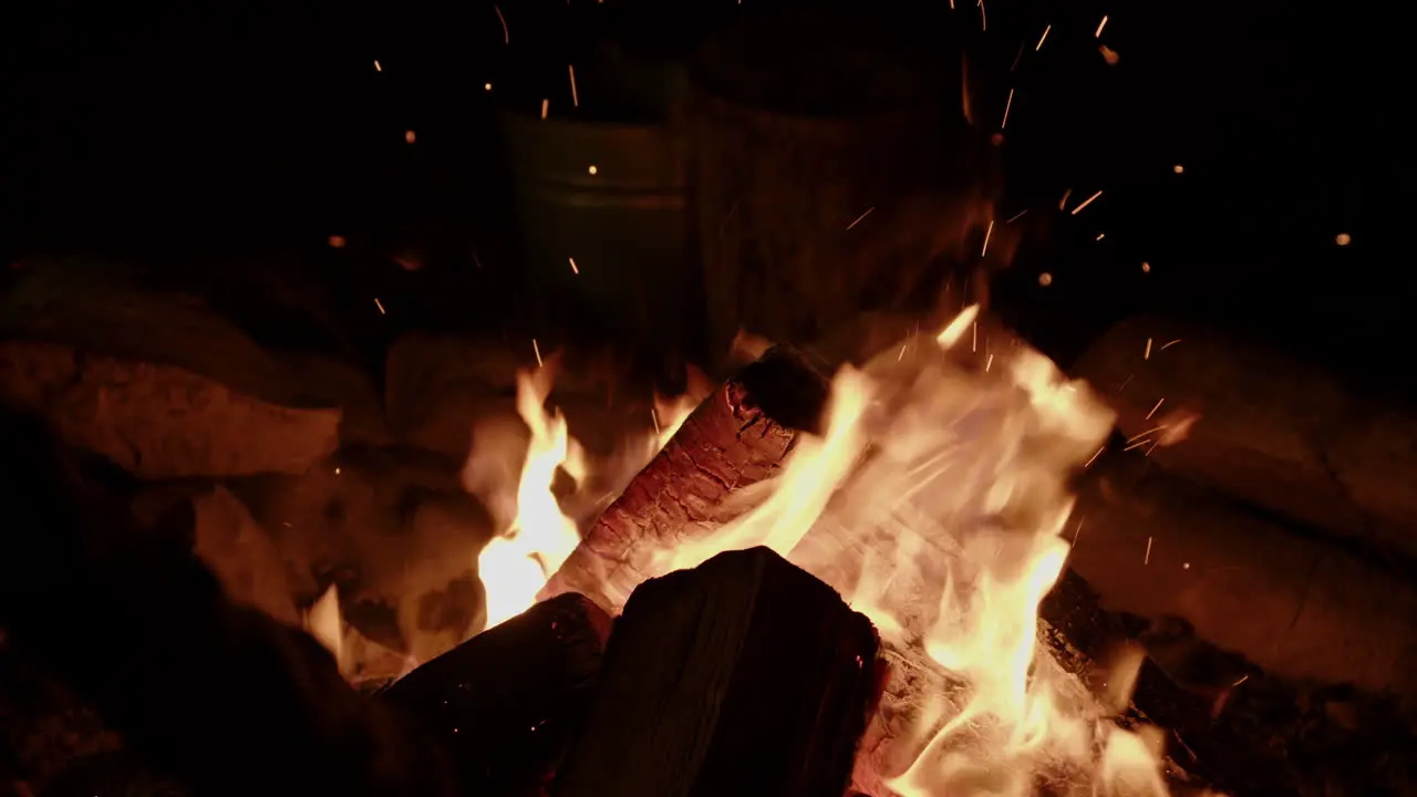 Slow motion close up of crackling campfire being tended to and embers flying off