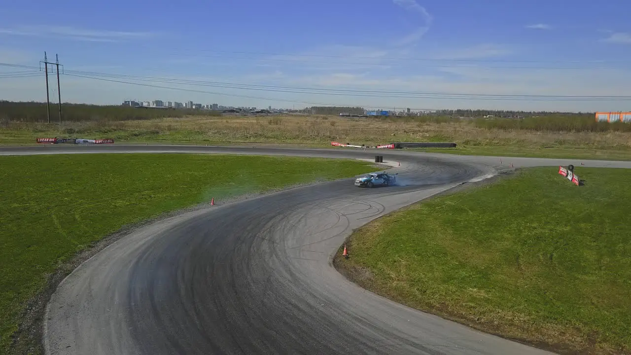 Aerial shot of a car drifring on high speed on a turn green grass and a race track top side shot