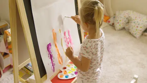 Little girl standing painting at an easel