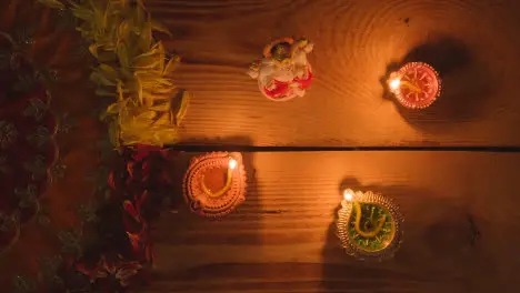 Blowing Out Diya Lamps On Table Decorated For Festival Of Diwali With Statue Of Ganesh