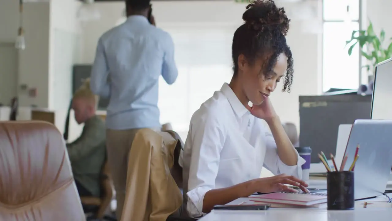 Happy african american businesswoman using laptop with colleagues in creative office