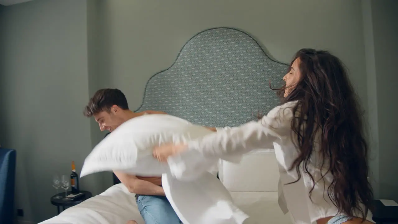 Couple smiling each other in hotel room Cheerful couple playing pillows on bed