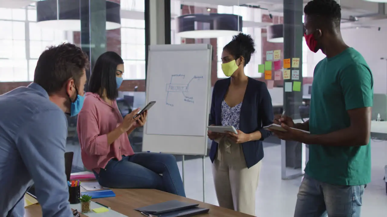 Mixed race business colleagues wearing face masks having a discussion in meeting room making notes