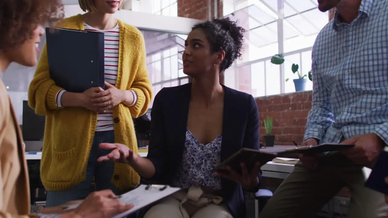 Mixed race businesswoman using tablet in office discussing with diverse colleagues