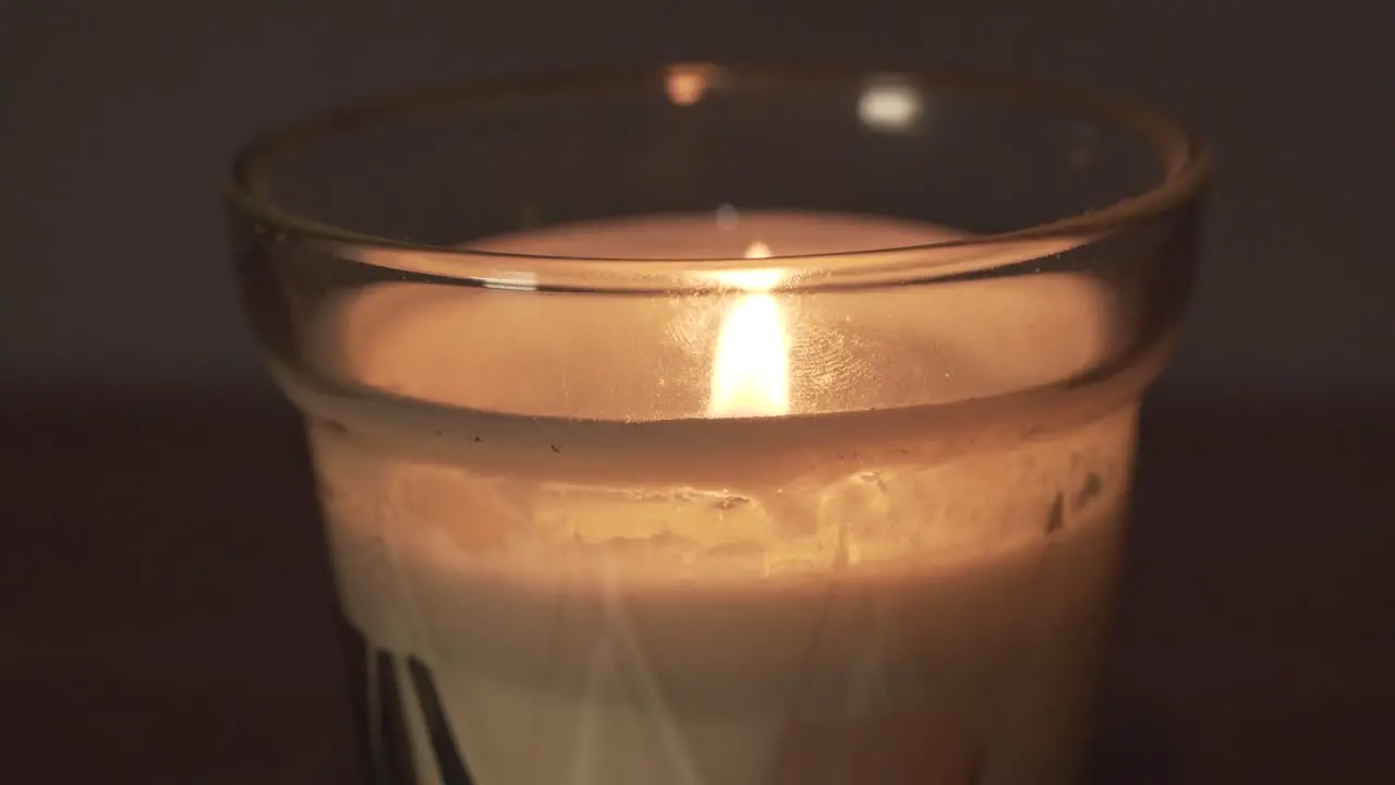 Close macro view of glass white wax candle and bright yellow flame at home