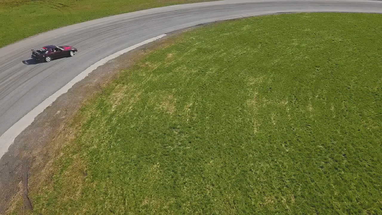 Aerial shot of a green car drifring on high speed on a turn green grass and a race track top side tracking shot