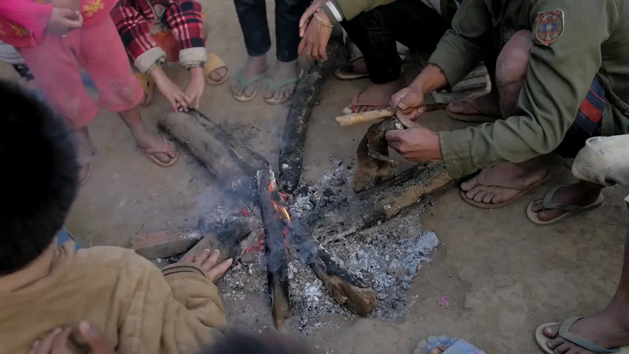 Laos village community cooking Loris animal over flaming bonfire in rural scene