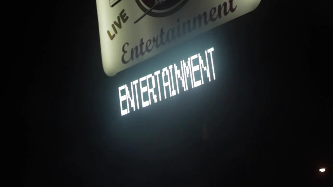 Hand-held Footage Of A Bright Neon Sign Attracting People Into The Stripclub