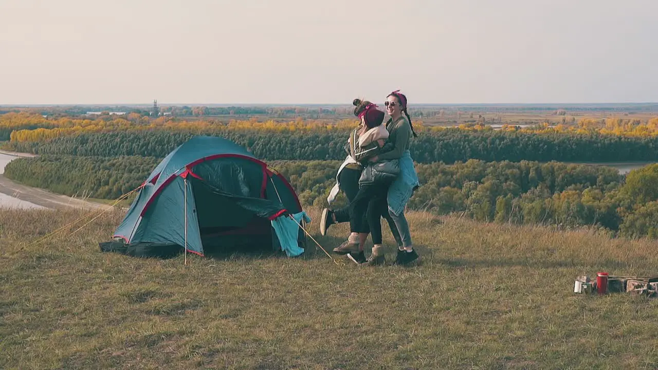 funny girls jump and dance between blue tent and campfire