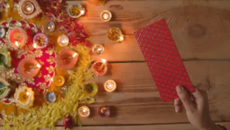 Overhead Shot Of Person Giving Gift Of Money With Burning Lamps Celebrating Festival Of Diwali